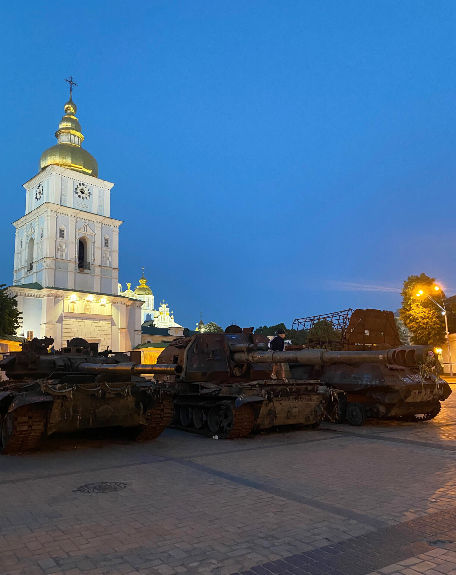 A young boy plays on a set of partially destroyed tanks placed in the center of Mykhailivska Square, Kyiv.